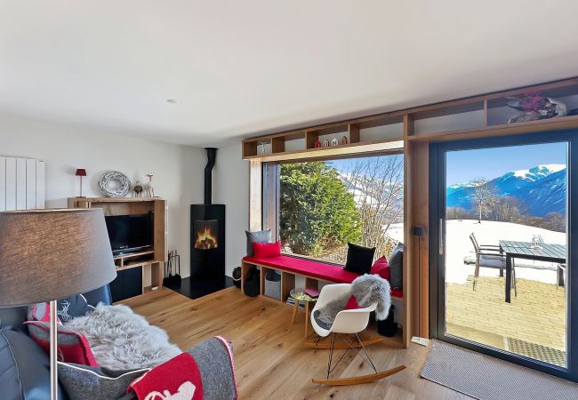 Wohnzimmer mit Kamin, gemütlichem Sofa, einladendem Sessel und großem Fenster mit Blick auf die Terrasse.