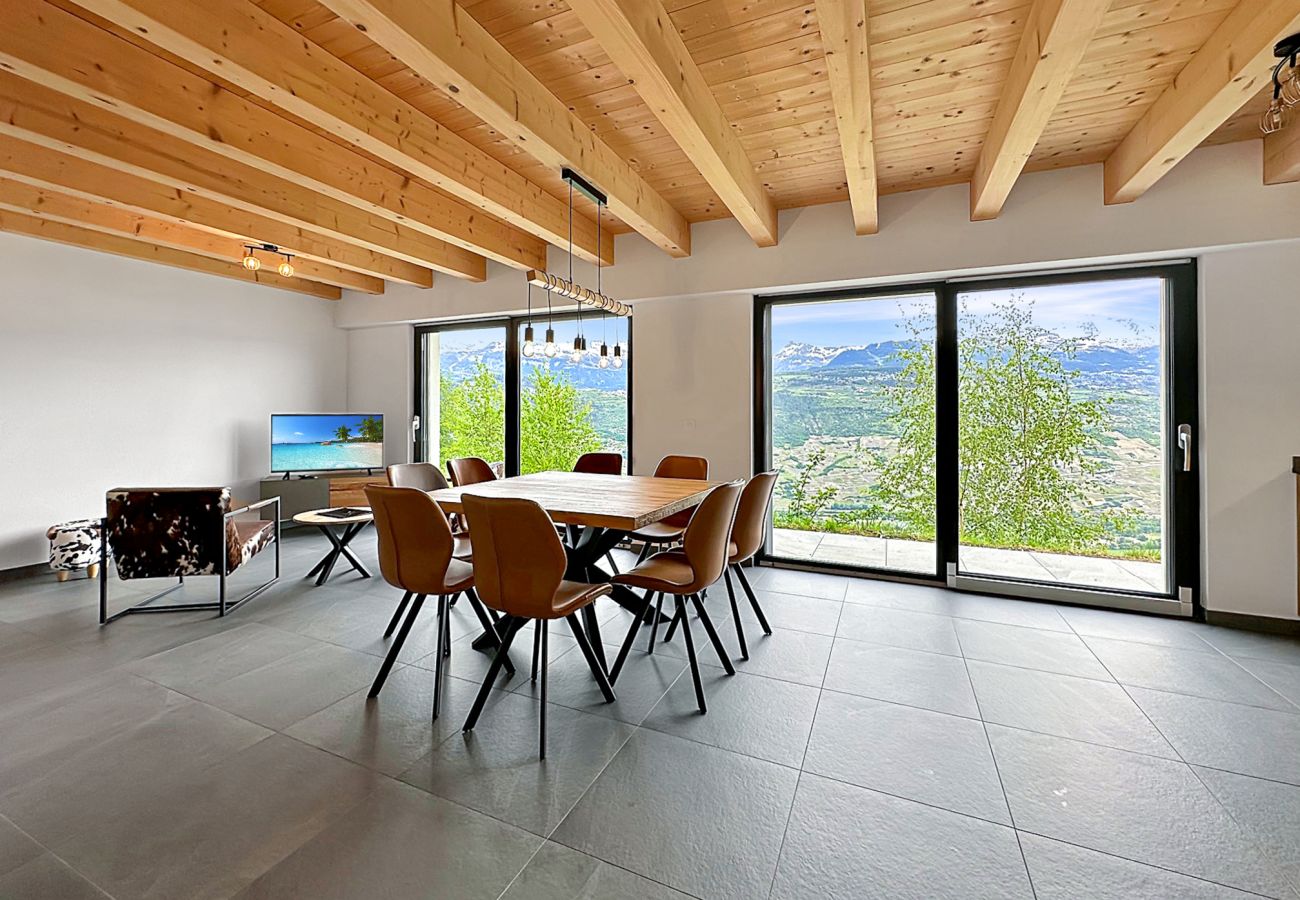 Grande pièce à vivre avec table à manger, fauteuils, télévision et grandes baies vitrées illuminant la pièce